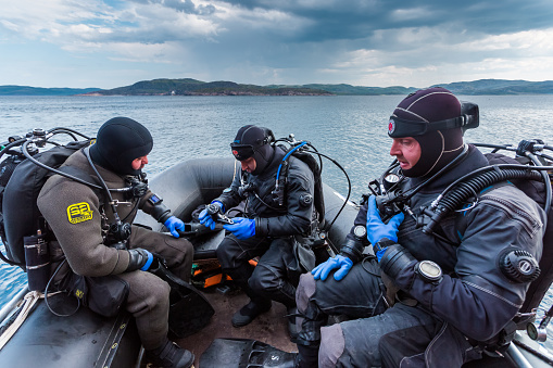 Teriberka, Russia - July 29, 2017: Three scuba divers sitting in the boat, checking their equipment and preparing to dive. Shot in Barents sea.