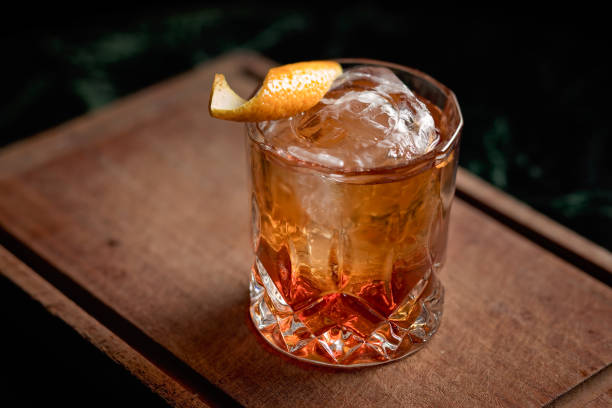 Old fashioned cocktail with an orange twist Old fashioned cocktail with an orange twist, an ice ball, present over a wooden board alcohol stock pictures, royalty-free photos & images