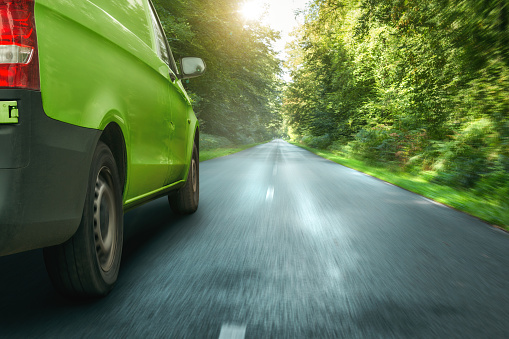 Green van on a forest road with lush vegetation. Motion blurred road.