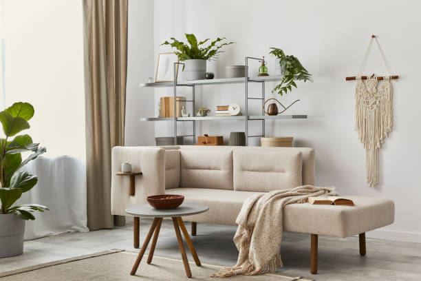 istock Cozy interior with stylish sofa, grey coffee table, bookcase, plants, carpet, decoration, beige macrame and elegant personal accessories. Neutral living room in classic house. Template. 1286688772