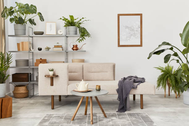 istock Cozy interior with stylish sofa, grey coffee table, bookcase, plants, carpet, decoration, mock up poster map and elegant personal accessories. Neutral living room in classic house. Template. 1286688785