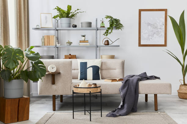 istock Cozy interior with stylish sofa, design coffee table, bookcase, plants, carpet, decoration, mock up poster map and elegant personal accessories. Neutral living room in classic house. Template. 1286688786
