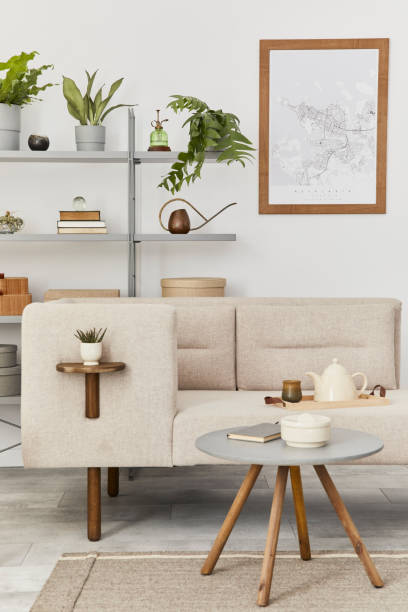istock Cozy interior with stylish sofa, grey coffee table, bookcase, plants, carpet, decoration, mock up poster map and elegant personal accessories. Neutral living room in classic house. Template. 1286688788