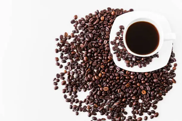 Photo of White cup with coffee and saucer, with scattered coffee beans on a white background. Great idea for a cafe, restaurant or cafeteria menu or as a sign