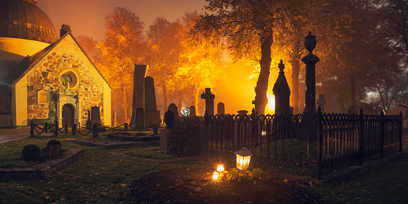 Evening view of a graveyard around All Saints Day. In the foreground candles and a lantern are lit at a grave. Norra begravningsplatsen, Stockholm.