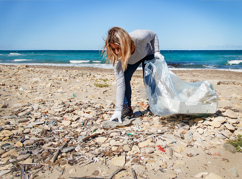 Young woman cleaning beach area from plastic  bottles