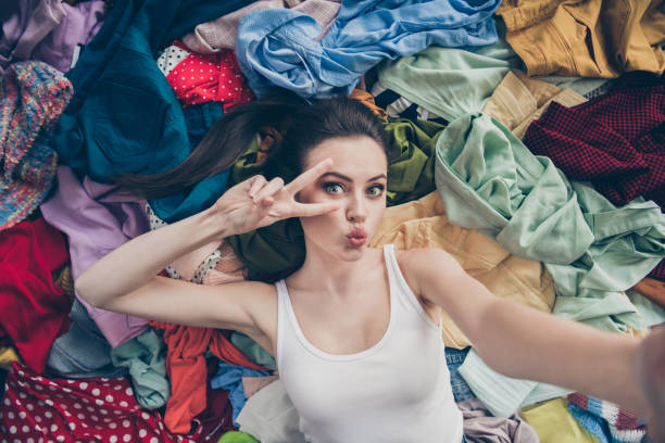 istock High angle above photo of lovely lady home spring cleaning lying many clothes stack floor prepared untidy stuff washing make selfies show v-sign symbol followers her stuff send kiss indoors 1286695708