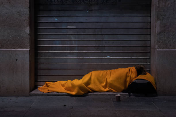 una persona sin hogar duerme en la calle bajo una manta frente a un escaparate - vagabundo fotografías e imágenes de stock