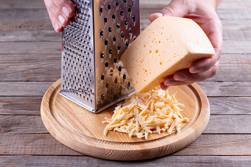 ooking, food and home concept - close up of male hands grating cheese on a cutting board