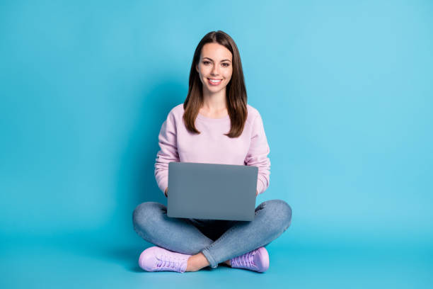 full length photo of pretty lovely student girl sitting floor crossed legs hold laptop freelancing copywriting chilling wear violet pullover sneakers denim isolated blue color background - shirt women pink jeans imagens e fotografias de stock