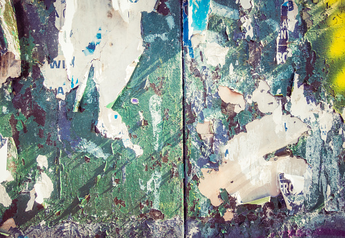 Close-up of an ageing urban surface, with fading and peeling paint, ripped paper