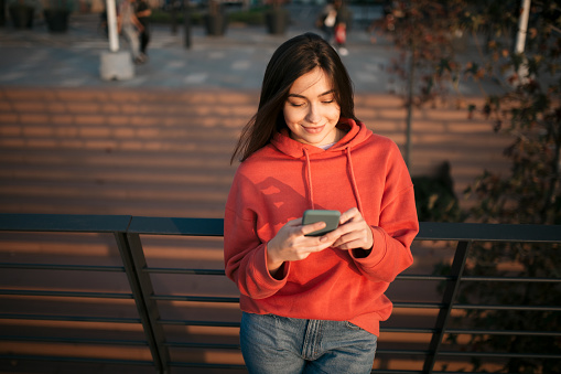 High angle view of a happy young Caucasian woman wearing a red shirt, relaxing outdoors and using a smart phone, smiling