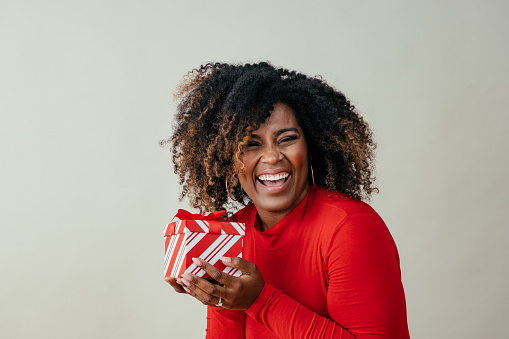 Caucasian girl is holding a gift box over her head and expresses happiness on white background