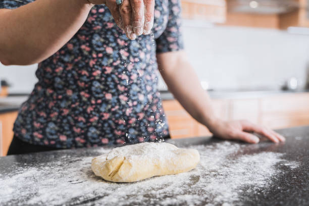 istock Woman sprinkling dough with flour in kitchen. 1286708753