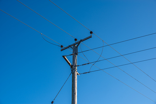 Wooden telegraph pole with wires and insulators with a clear blue sky background