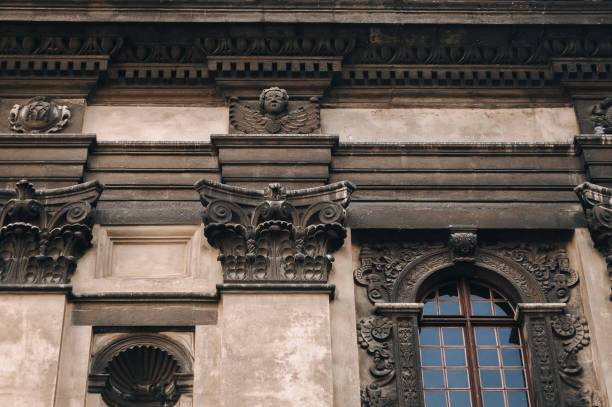 istock Antique baroque window with iron bars framed by decorative stucco on a gray wall with capitals. The Jesuit Church in Lviv. 1286709664