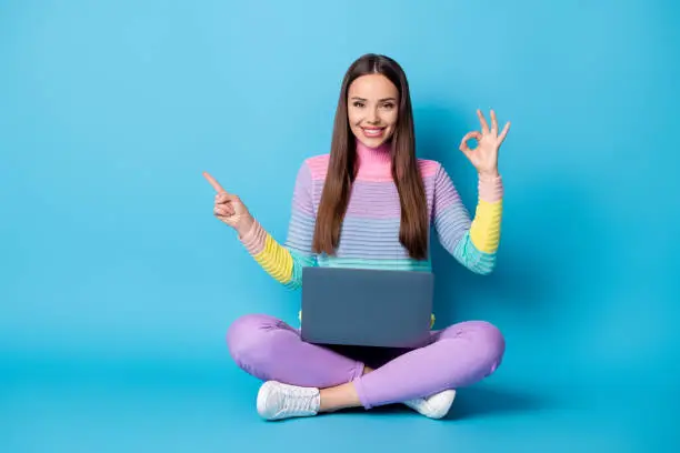 Portrait of attractive cheerful girl sit lotus position crossed legs using laptop showing ok-sign copy space isolated on bright blue color background.