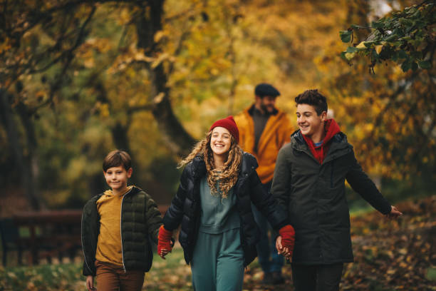 istock Sister and two brothers are holding hands, walking on forest path. Autumn time. 1286713201