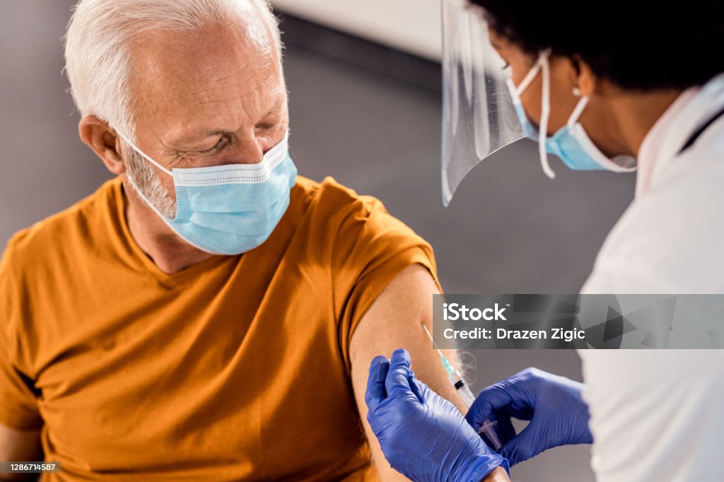 Senior man wearing face mask while receiving vaccine at medical clinic. Male senior patient getting vaccinated at medical clinic during coronavirus pandemic. Vaccination Stock Photo