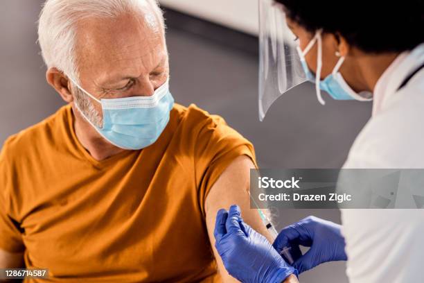 Senior Man Wearing Face Mask While Receiving Vaccine At Medical Clinic Stock Photo - Download Image Now