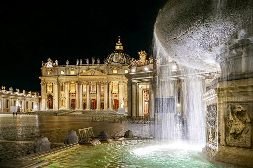 Vatican, Italy, January 09 - Night view of the facade of St. Peter's Basilica with the reflections on the water of a Bernini fountain. St. Peter's Basilica, in the Vatican, is the center of the Catholic religion, one of the most visited places in the world and in Rome for its immense artistic and architectural treasures. Photos in HD format
