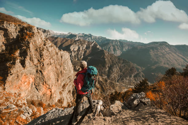 istock Hiker man with backpack standing on edge of cliff and looking at the mountains 1286715003