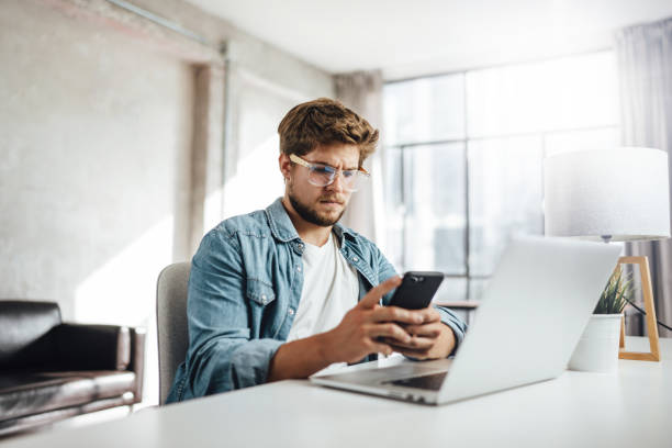 istock Young man with smartphone in his hands. Modern businessman at sunny office. Freelancer at work. 1286716305