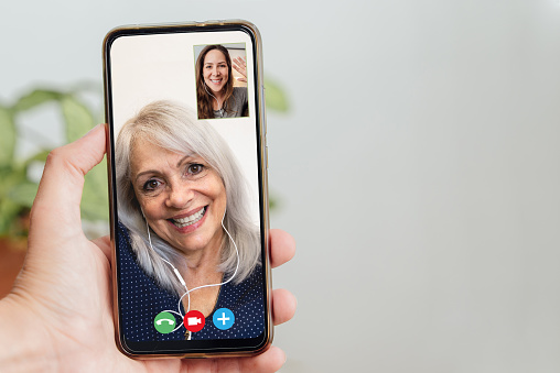 Happy senior and daughter talking on video call with mobile phone during coronavirus outbreak - Online app and social distancing concept