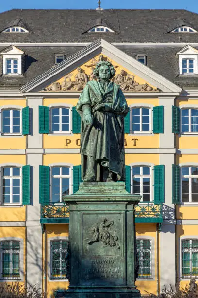 A statue of famous composer Ludwig van Beethoven - with the beautiful Old Post Office building in the background, located on Munsterplatz in the city of Bonn in Germany.