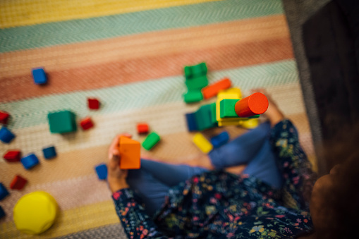 Aerial view of a mixed race girl building a tower with building blocks at home.