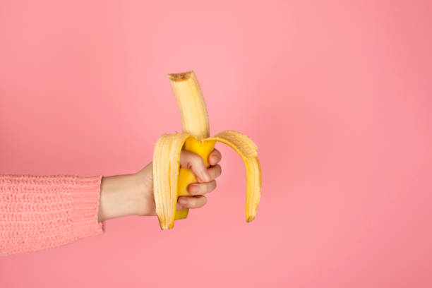 la mano femminile tiene la banana morsa gialla brillante - mature women isolated mature adult women foto e immagini stock