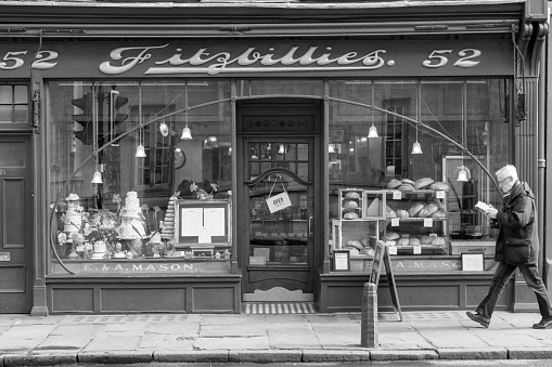 People sit inside the well-known Fitzbillies, a traditional bakery and café on Trumpington Street in Cambridge, England. There is a man walking past reading a book