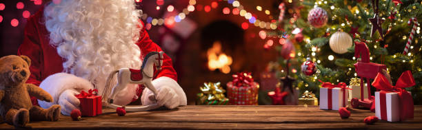 der weihnachtsmann sitzt an einem tisch mit geschenken und spielzeug - werkstatt stock-fotos und bilder