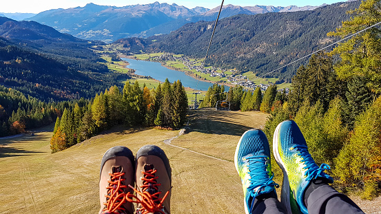Two pairs of hiking shoes on the slope with the view on a distant Weissensee lake. The grass on the slopes is golden, trees also change colors to yellow and orange. High Alps around. Autumn vibes