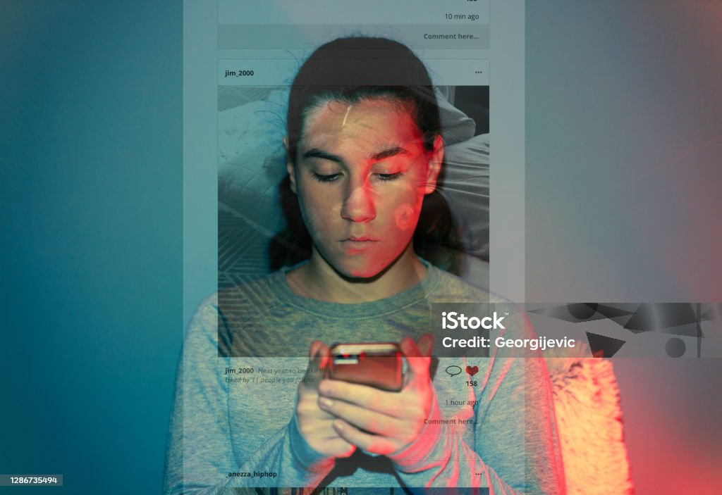 The Social Media Overuse A 13-year-old girl is using her smartphone in the dark room. The content she is browsing projects over her face and wall behind her. Social Media Stock Photo