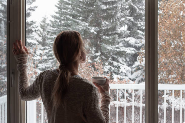istock Woman looking out window holding coffee cup, winter outside 1286737016