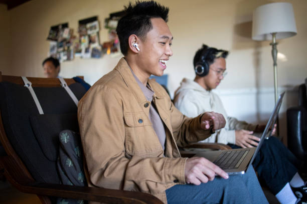 dos hermanos filipinos en ordenadores portátiles en livingroom - filipino ethnicity audio fotografías e imágenes de stock