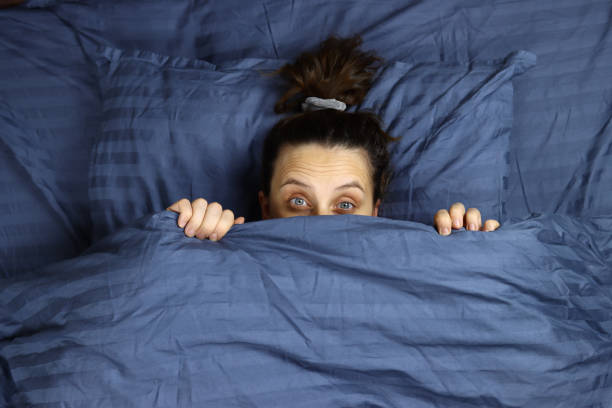 istock Young girl looks out from under the covers lying in bed 1286745041
