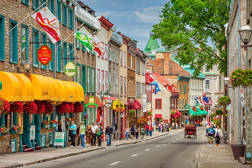 People walk past colorful store fronts and restaurants on Rue Saint-Louis in old town Quebec City, Canada on a sunny day.
