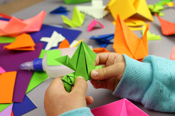 istock Child makes origami crafts from colored paper, hands close-up 1286746361