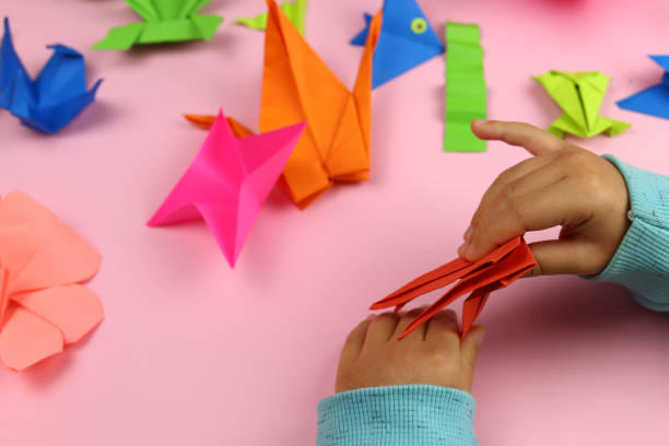 istock A child makes origami from colored paper on a pink background 1286746444