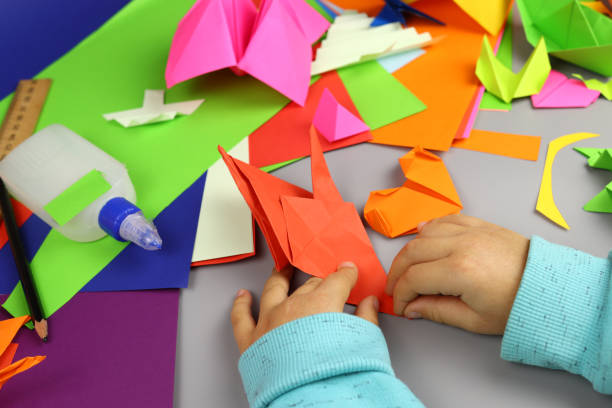 istock Child makes origami crafts from colored paper, hands close-up 1286746463