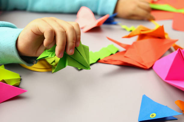 istock Child makes origami crafts from colored paper, hands close-up 1286746468