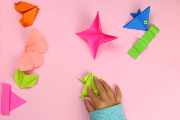 istock A child makes origami from colored paper on a pink background 1286747077