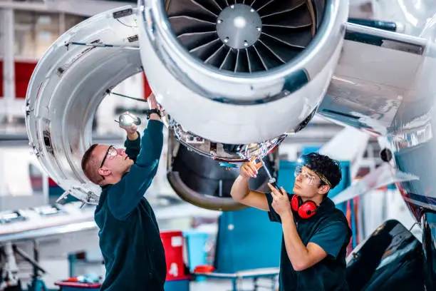 Two maintenance engineers checking and inspecting an airplane jet engine using the work tool in the hangar.