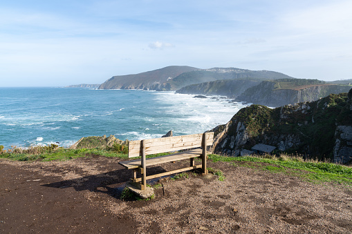 A scenic viewpoint with wooden bench on beautiful ocean coast with high cliffs and big waves
