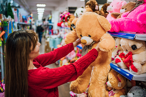 Young cheerful woman choosing teddy bear in a toy store