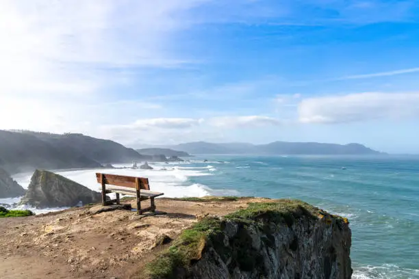 Photo of scenic viewpoint with wooden bench on beautiful ocean coast with high cliffs and big waves