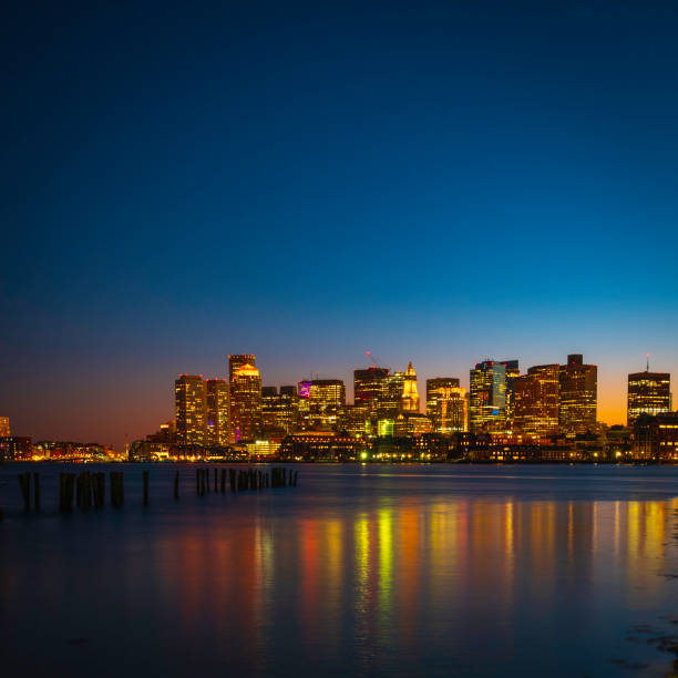 Modern Vibrant City Boston Skyline and Boston Harbor Water Reflections at Night Nightscape of the modern metropolitan city of Great Boston over the Boston Harbor water at twilight. Glittering lights of the city buildings reflected on the Mystic River water. east boston stock pictures, royalty-free photos & images