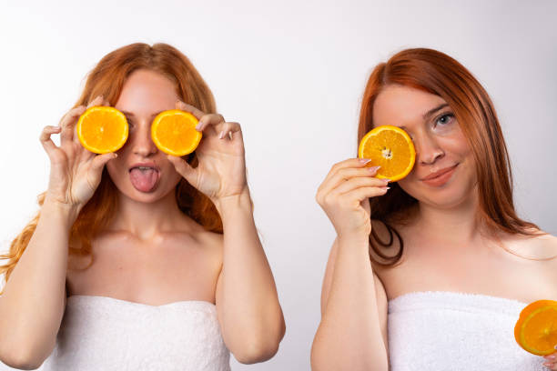 ragazze dal pelo rosso che si divertono con fette d'arancia. foto su sfondo bianco. - human lips orange lipstick human mouth foto e immagini stock